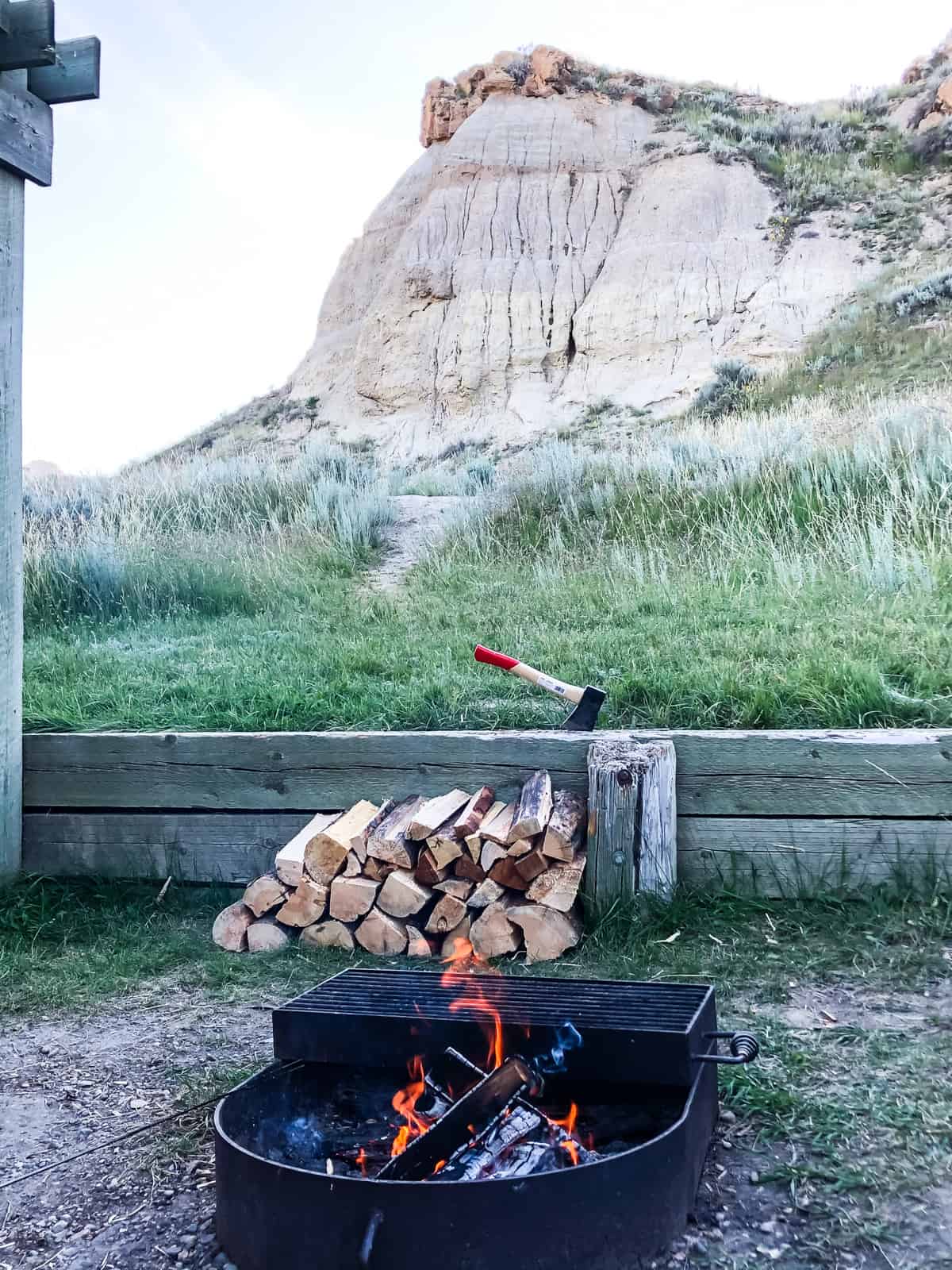 A campfire with stacks of firewood in the background